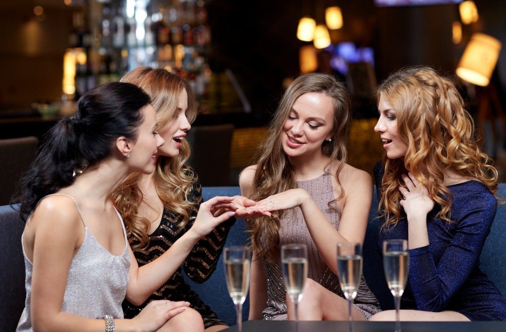 happy woman showing engagement ring to her friends with champagne glasses