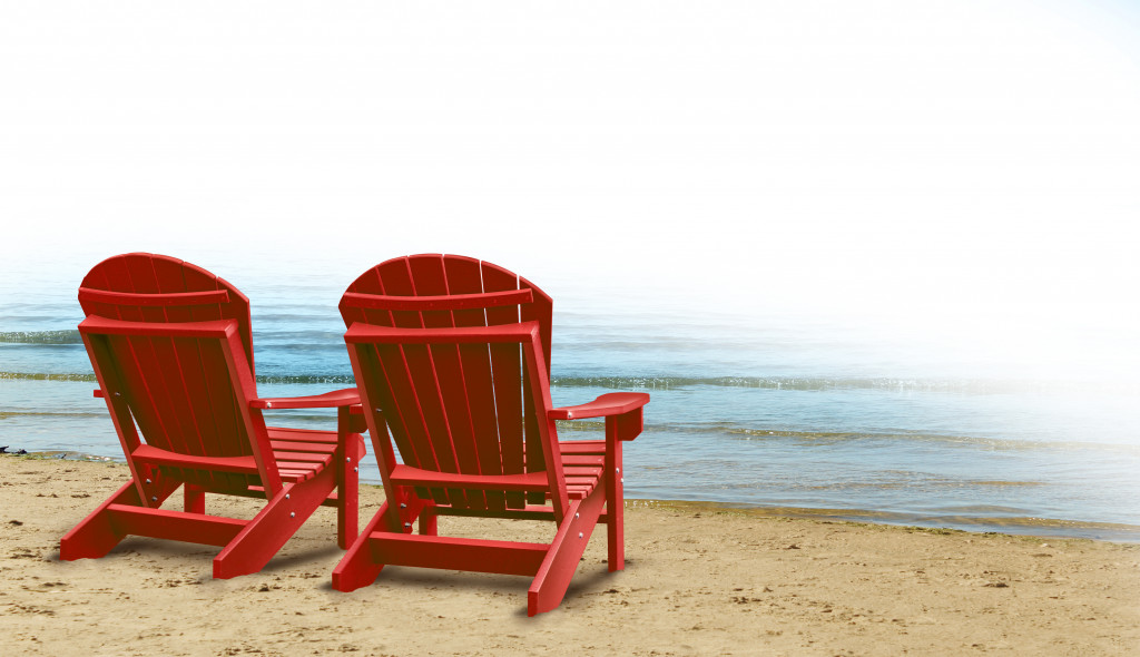 Two red chairs on a sandy beach with a good view of the ocean.
